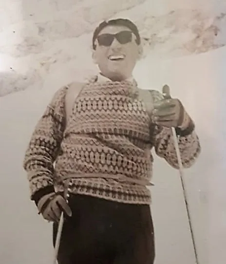 Teresio in the mountains wearing a patterned sweater and sunglasses, holding ski poles